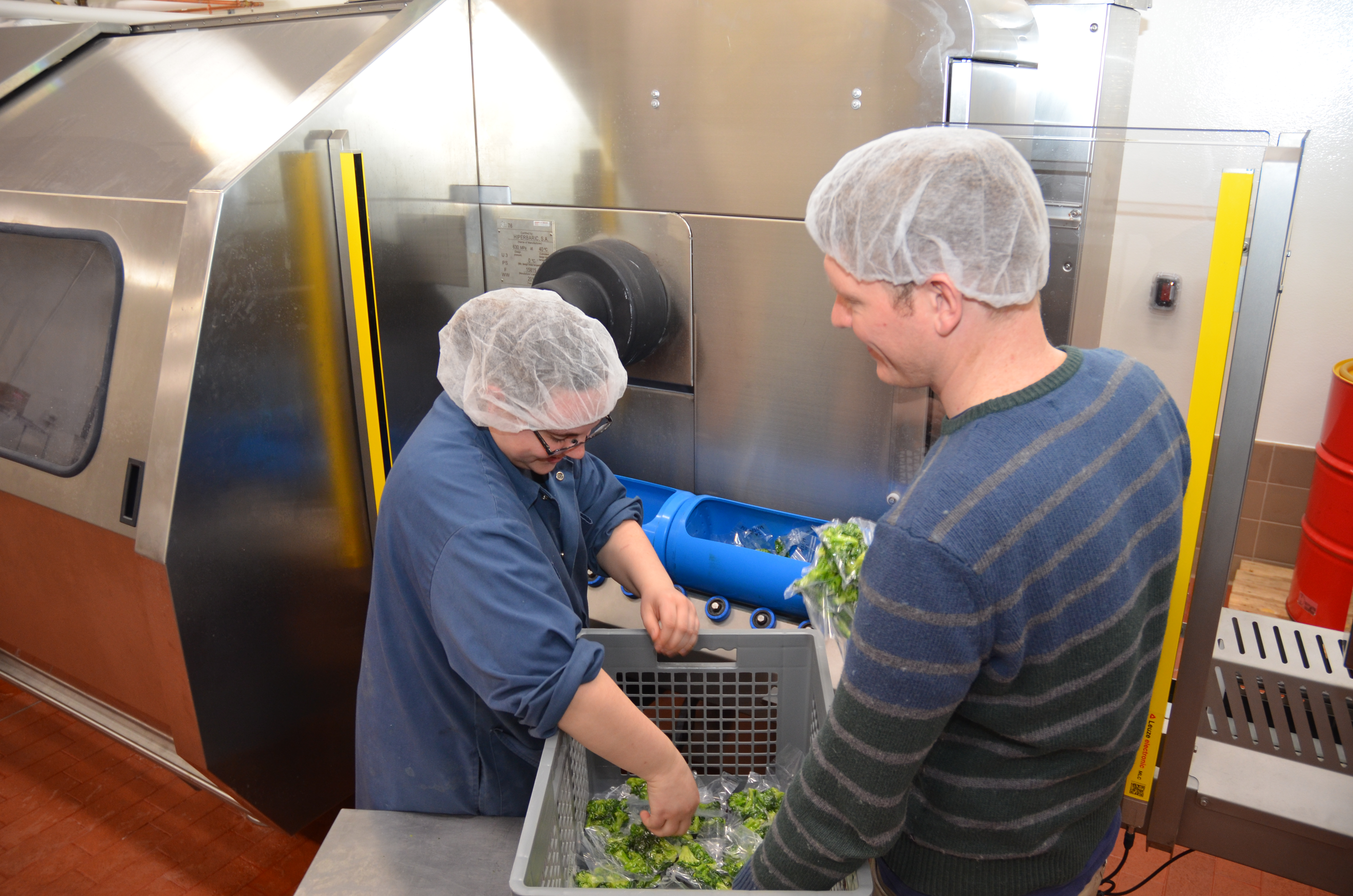 Two people loading brocolli into an High-Pressure Food Processor. 