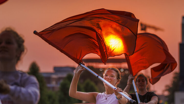 The rising sun appears to burn a hole through the flag of Cornhusker Marching Band color guard member Jaedynn Shively, a sophomore from Lincoln. 